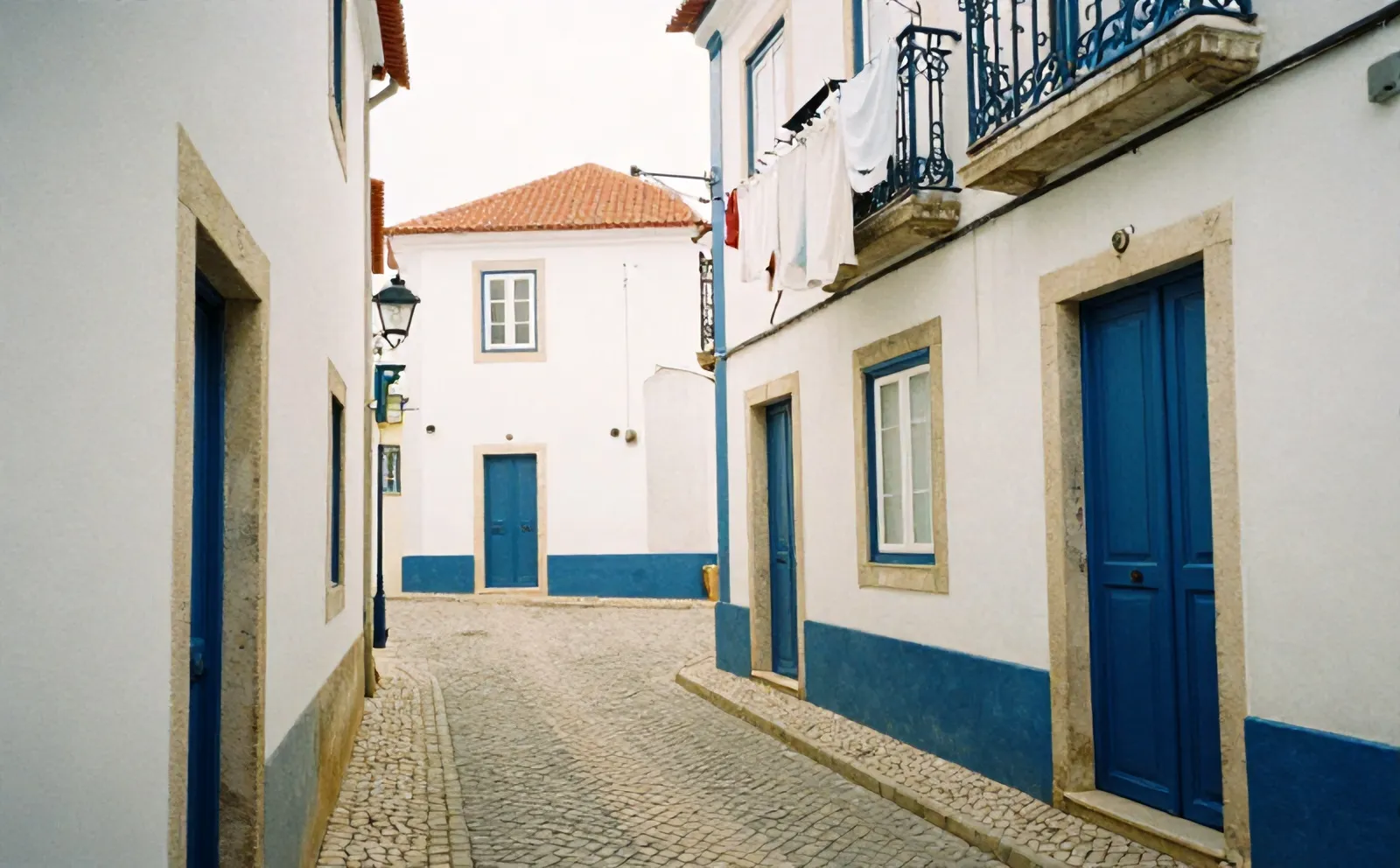 A narrow cobbled street in Ericeira old town with whitewashed walls and blue door frames