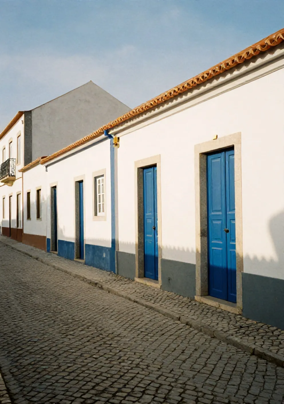 A cobbled lane in Ericeira old town between whitewashed houses with blue door frames