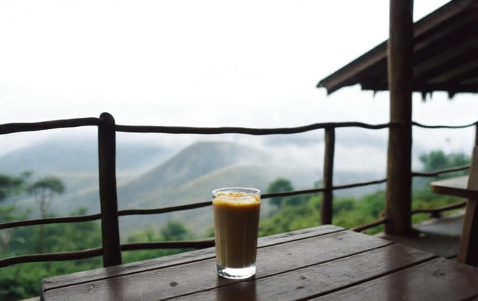Es kopi susu gula aren di meja teras dengan kabut di lereng Merapi