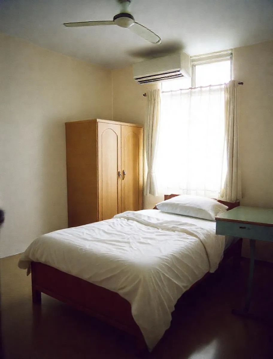 Kamar kos dengan kasur, lemari, dan meja belajar dekat jendela