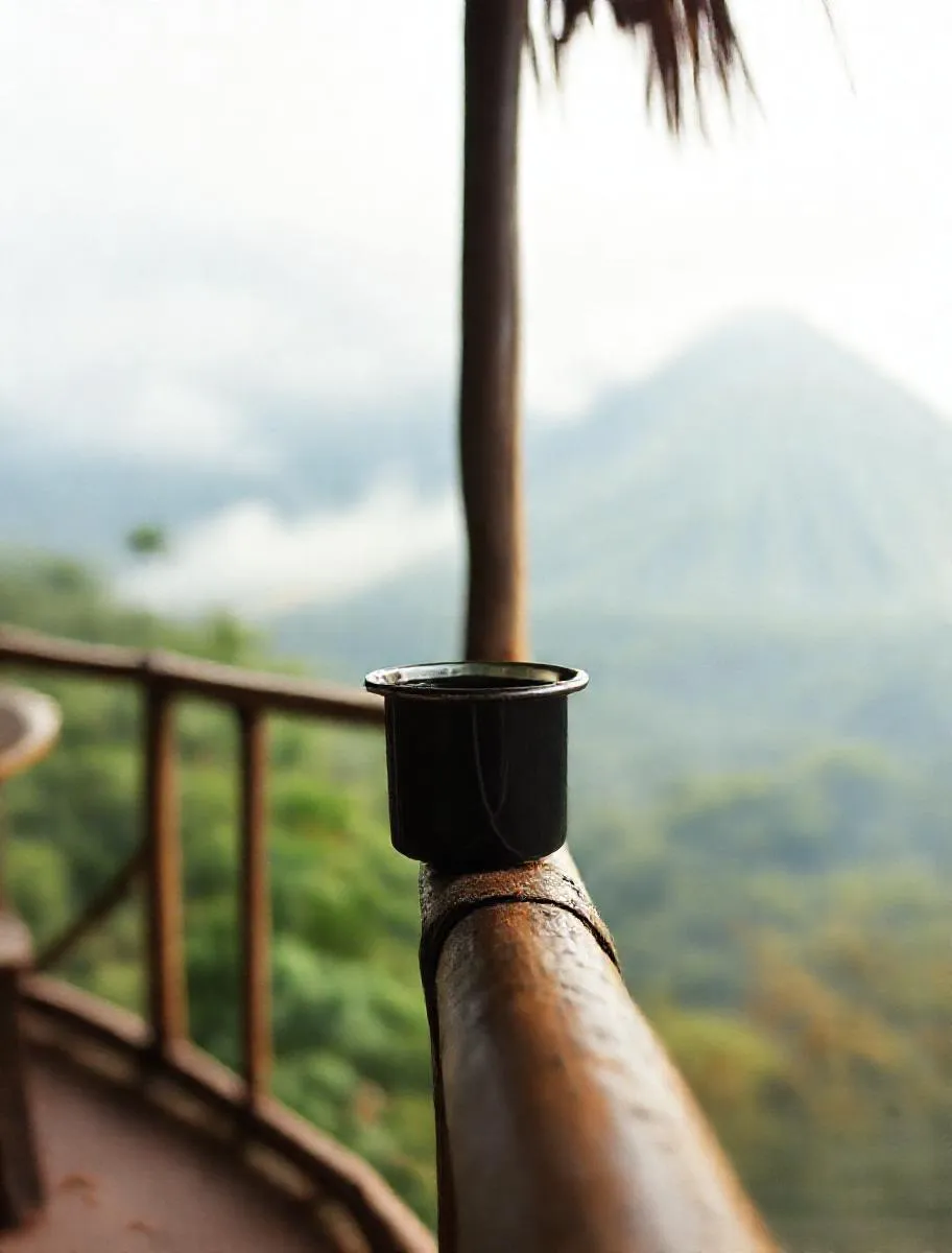 Secangkir kopi tubruk di pagar bambu teras, Merapi samar di belakang