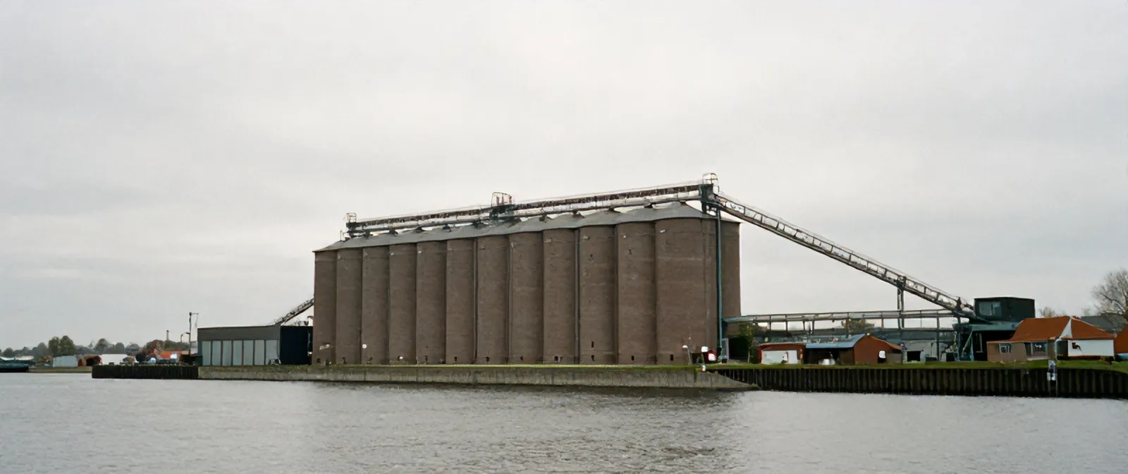 The Maassilo grain silo across the Maashaven water, brick cells and a steel conveyor bridge under a grey sky