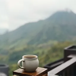 Cangkir kopi di pagar kayu teras dengan lereng berkabut