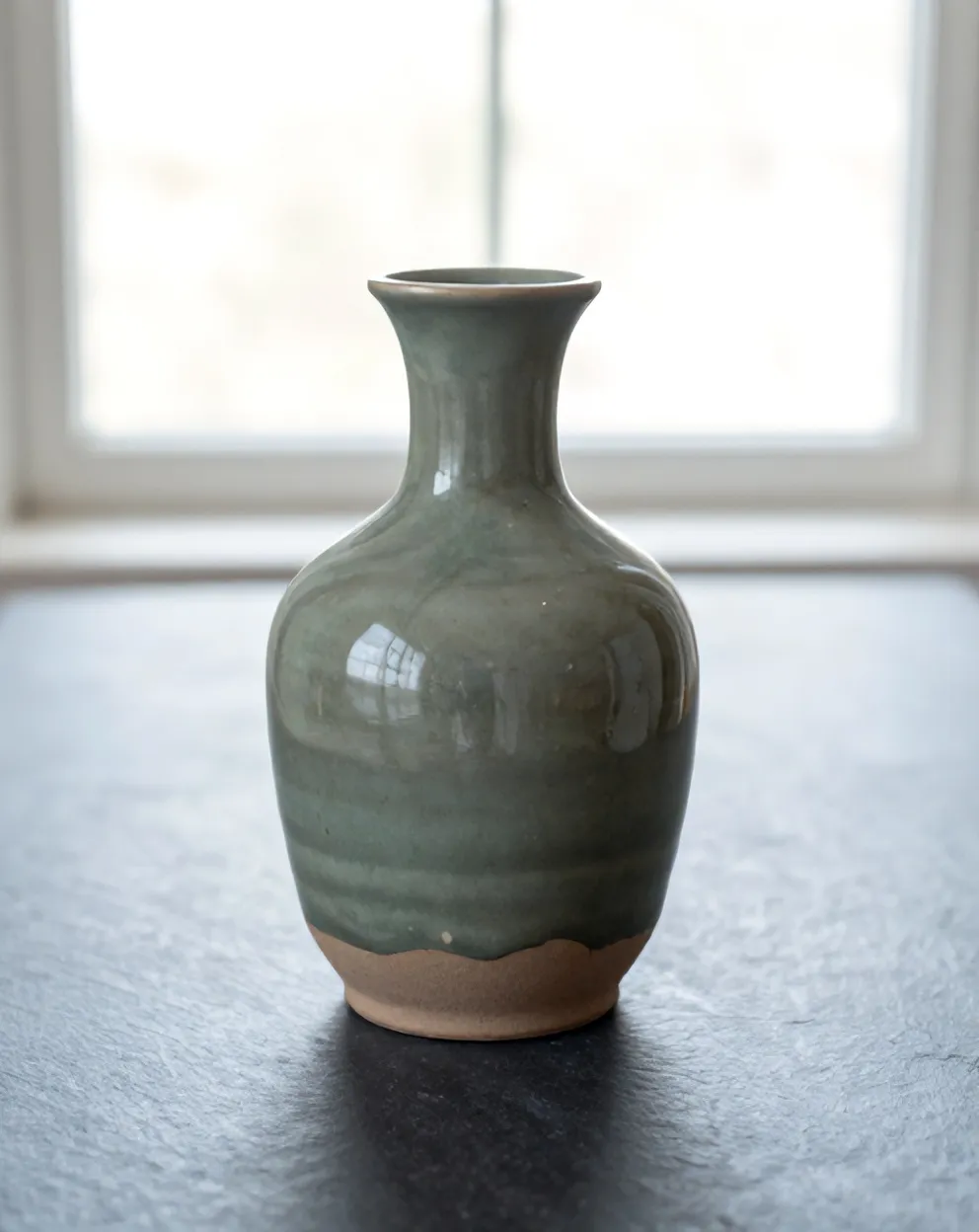 Slate glaze pooling darker at the foot of a carafe, above the bare clay ring