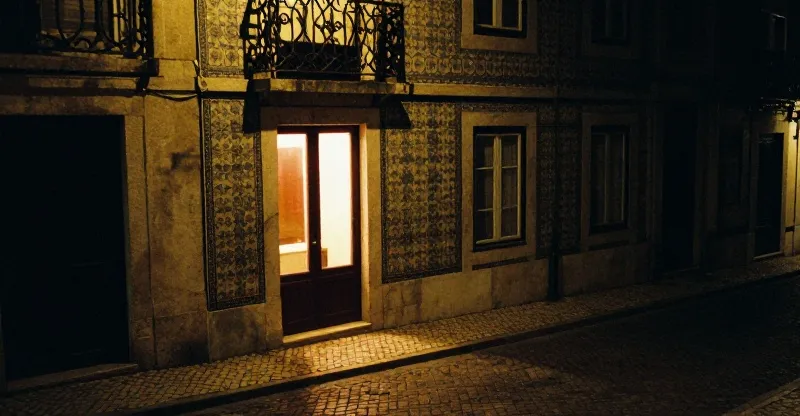 A steep cobbled lane in Alfama at night with one lit doorway