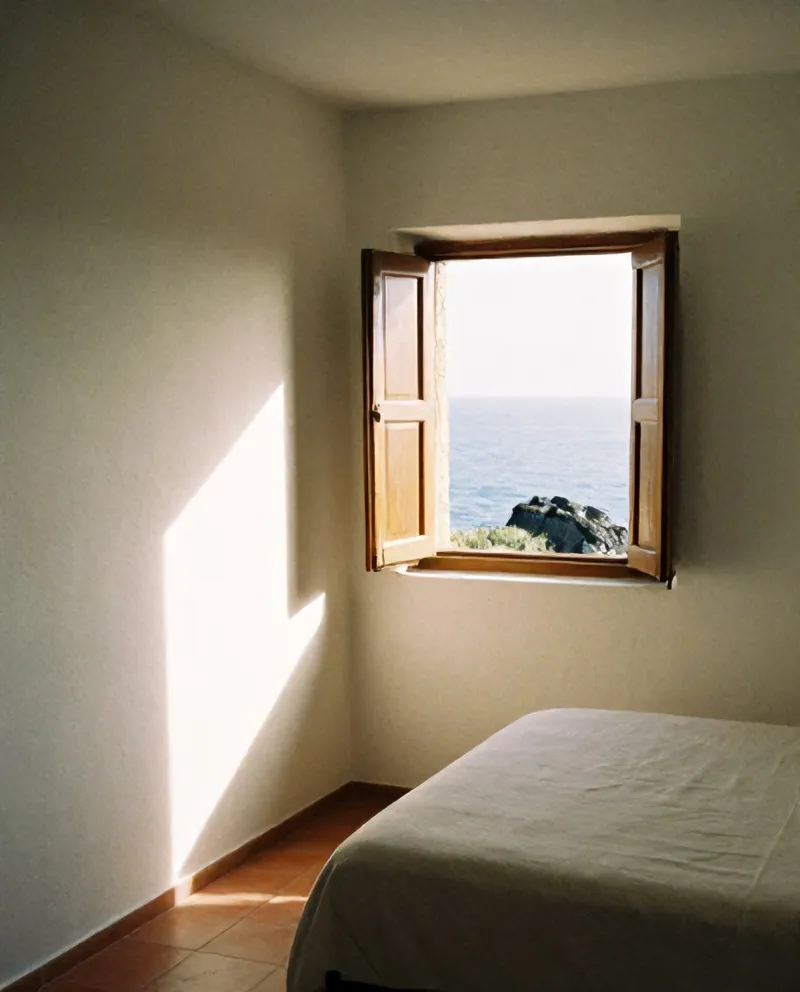 Room with linen bed and shutters open to the sea