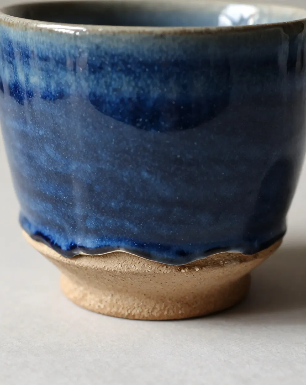 Blue glaze pooling and breaking to oatmeal at the bare clay foot ring of a Kiln cup