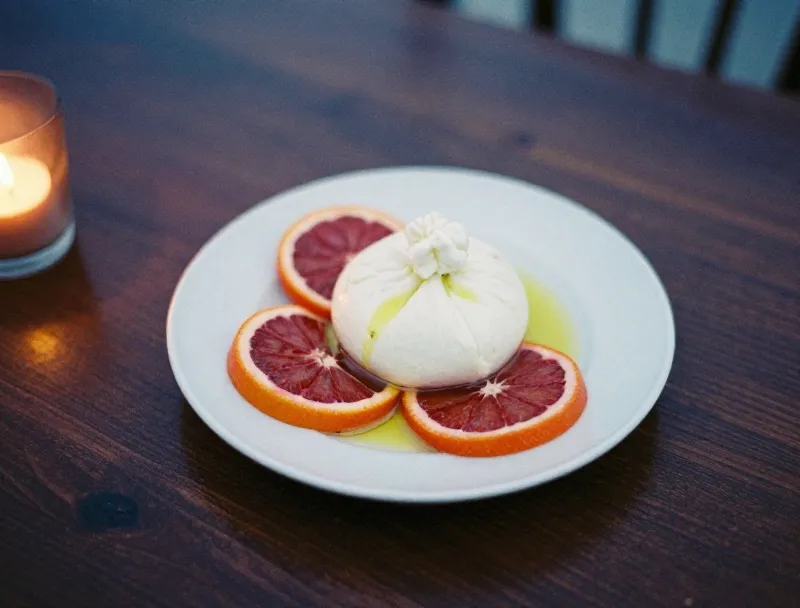 A plate of burrata with blood orange and olive oil on a wooden table