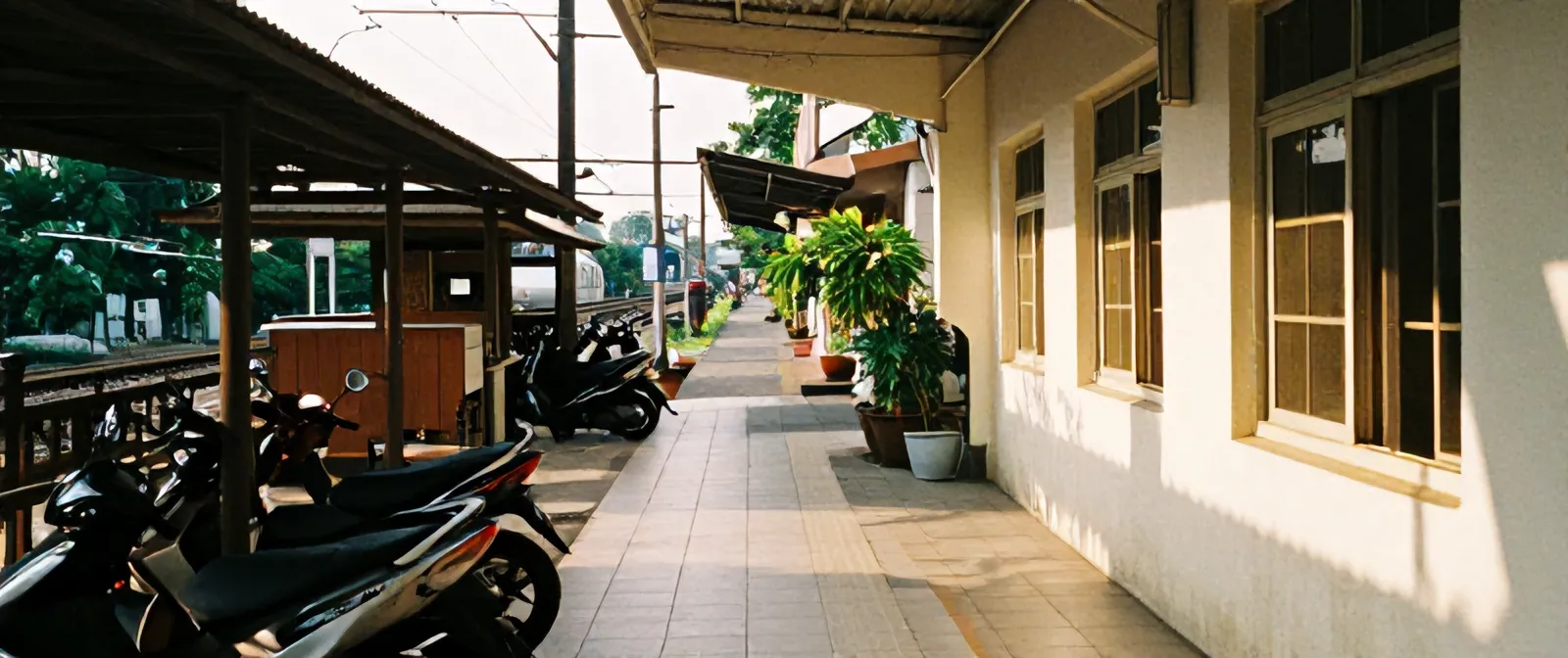 Gang sempit dekat Stasiun Pondok Cina dengan motor terparkir, warung, kabel listrik, dan KRL di ujung jalan