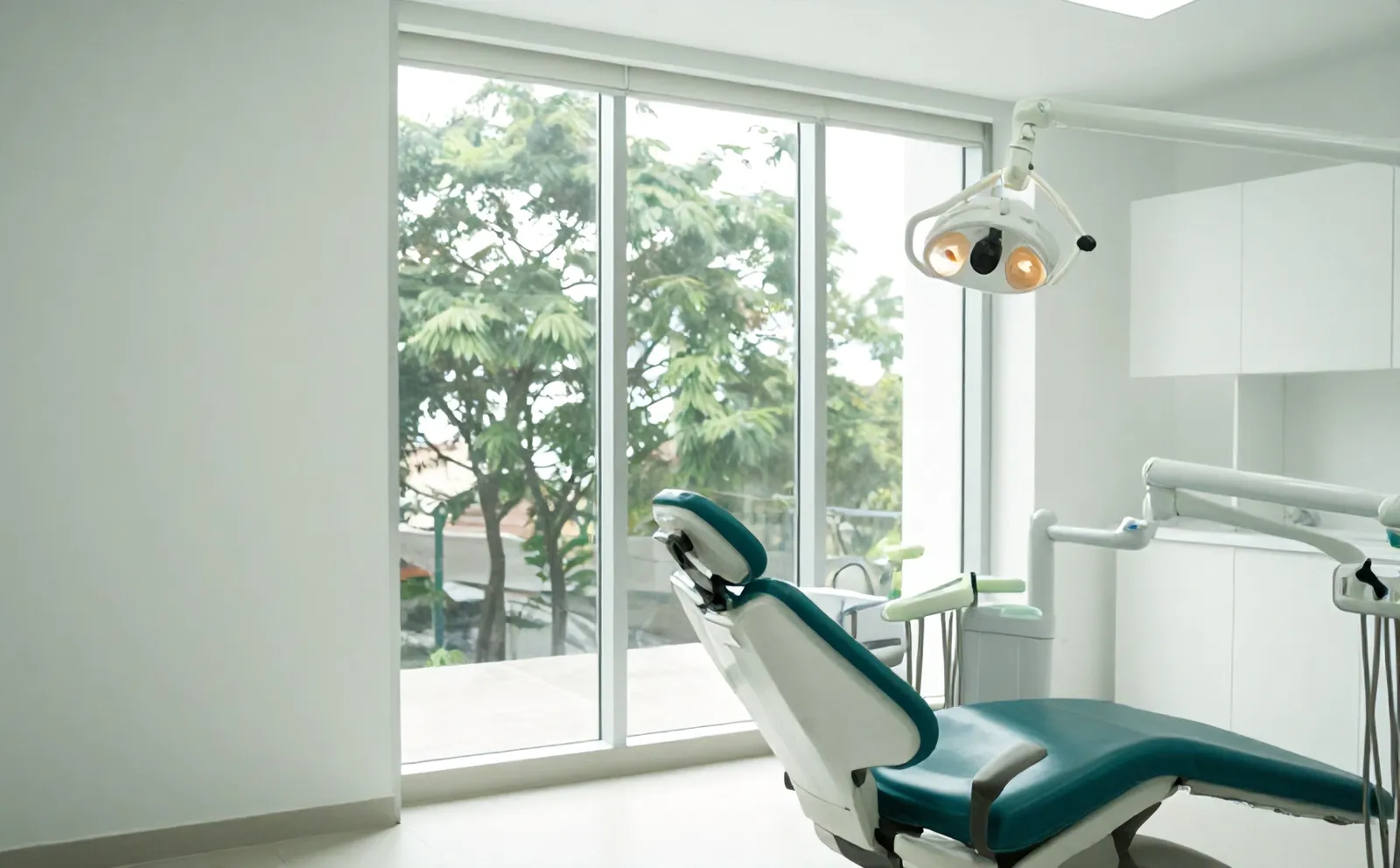 Ruang periksa Klinik Gigi Senyum Seri dengan kursi gigi teal dan jendela ke pohon trembesi Jl. Raya Darmo