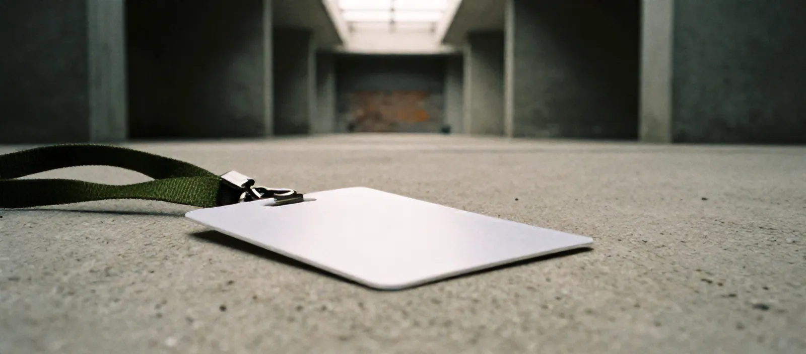 A blank white name badge on a moss green lanyard on raw concrete