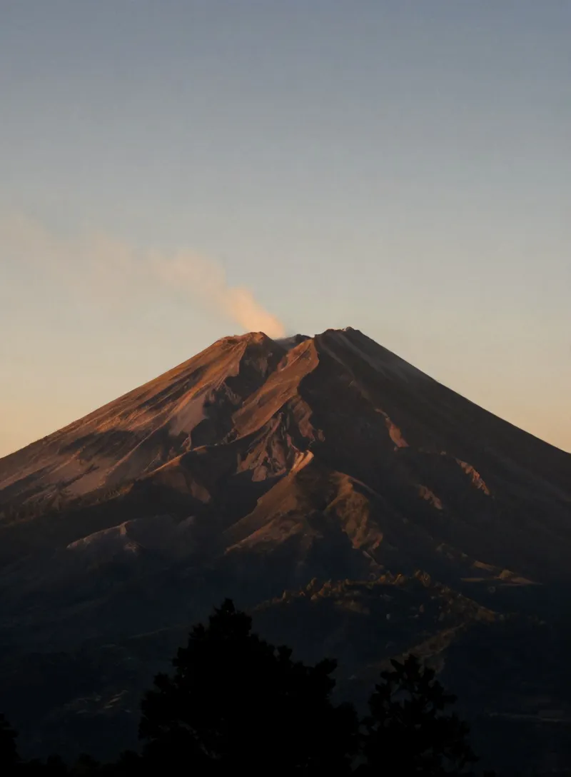 Puncak Merapi saat fajar di atas lereng pinus Kaliurang, asap tipis mengepul