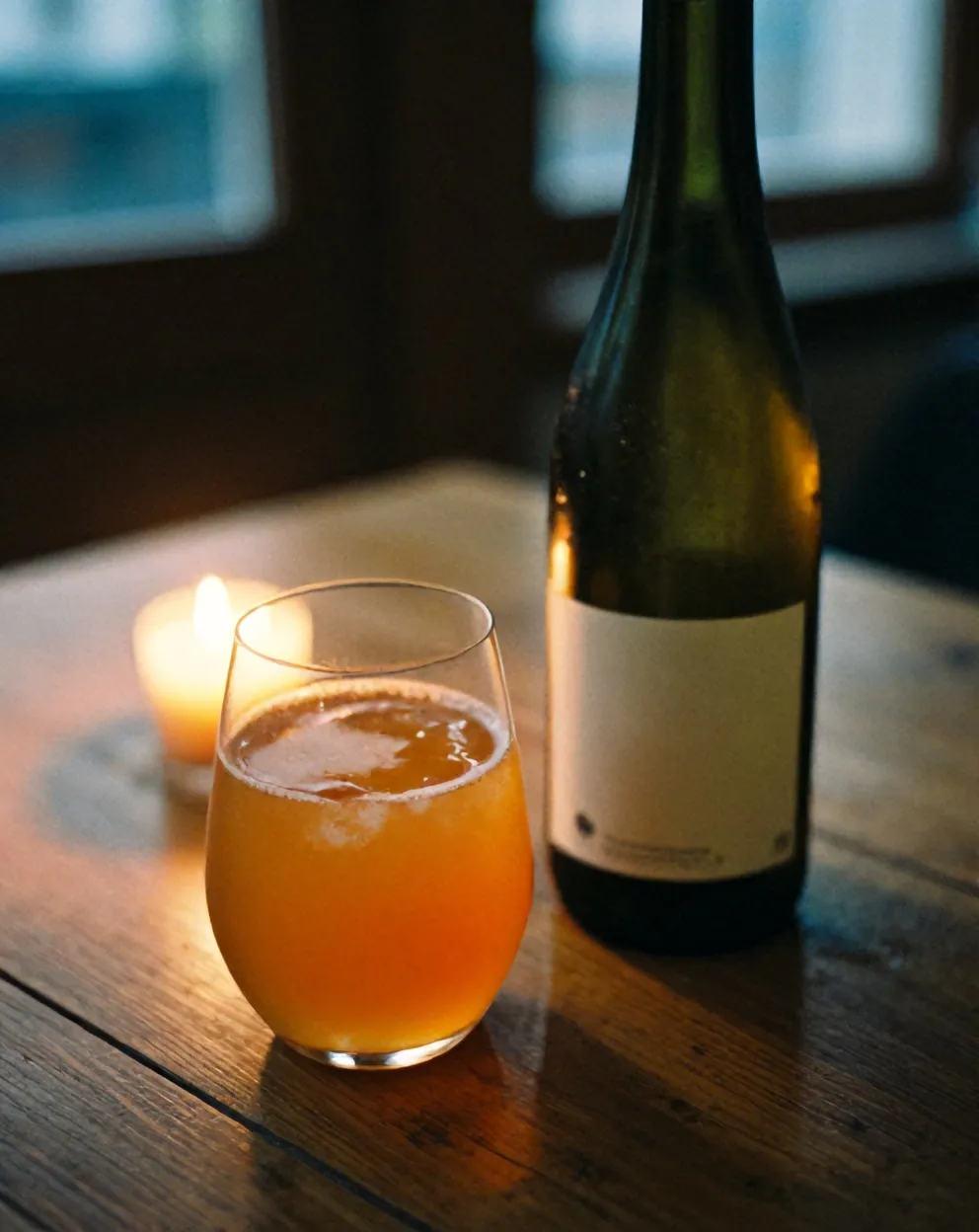 Orange natural wine in a tumbler beside an unlabelled bottle