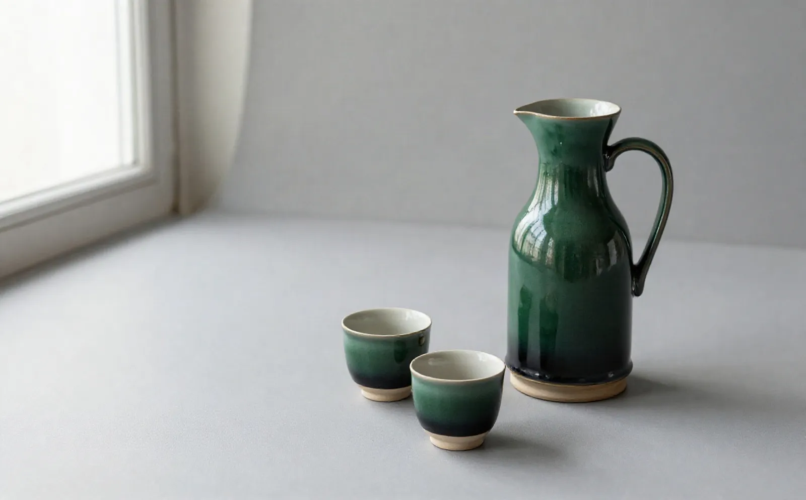 Two green cups filled with coffee beside the carafe, the glaze pale on the rims and dark at the foot