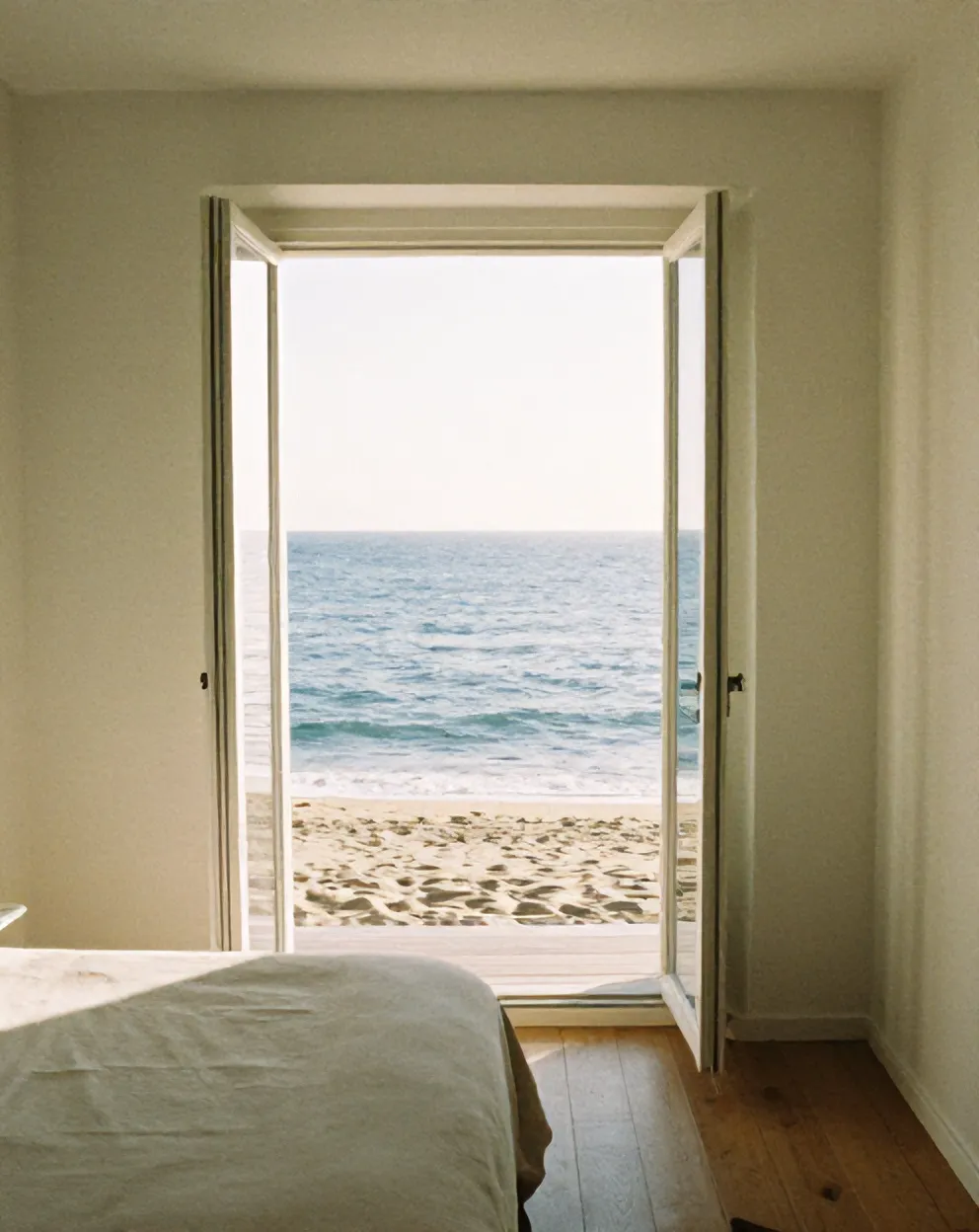 A white guest room with linen bed and a deep window onto the Atlantic