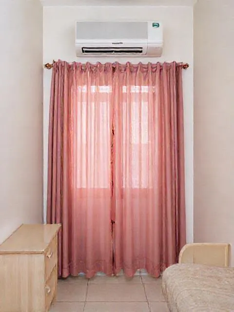 AC split di dinding kamar, di atas jendela bertirai tipis