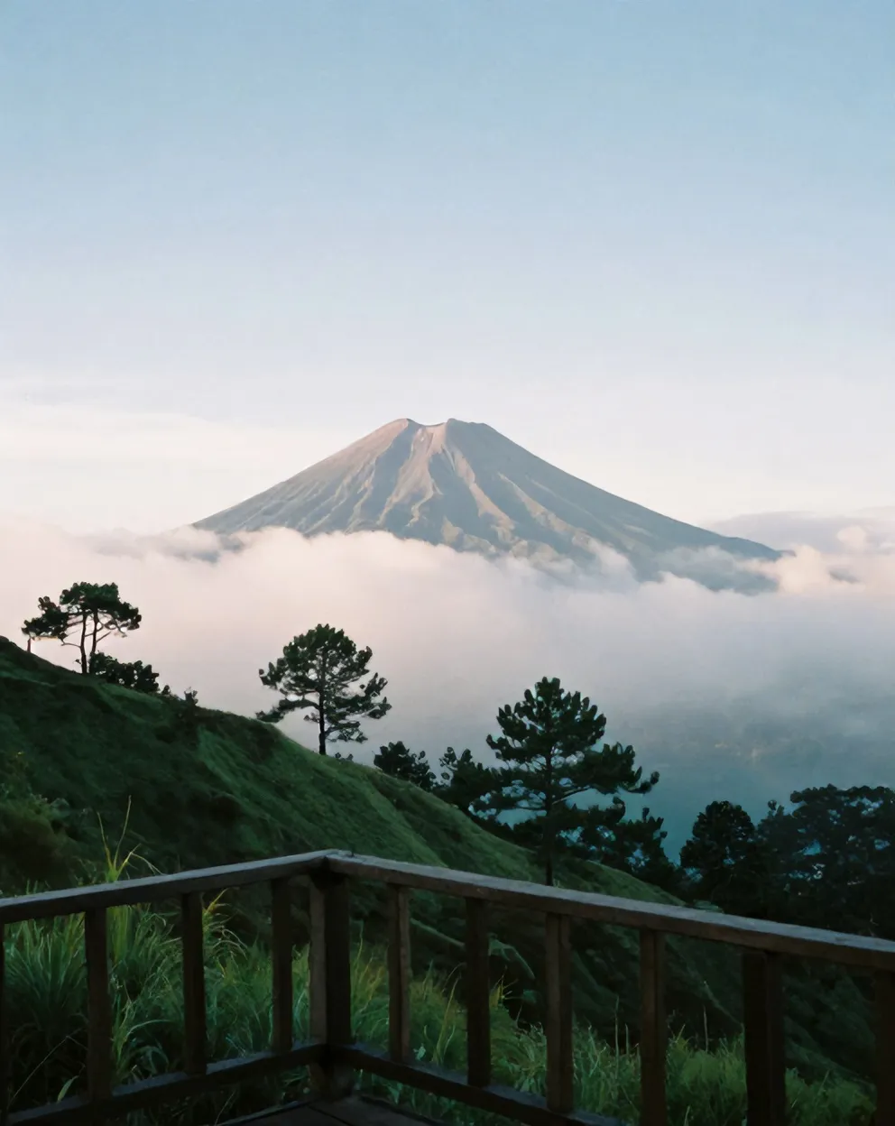 Puncak Merapi muncul dari balik awan pagi, dilihat dari pagar kayu teras Kopi Lereng