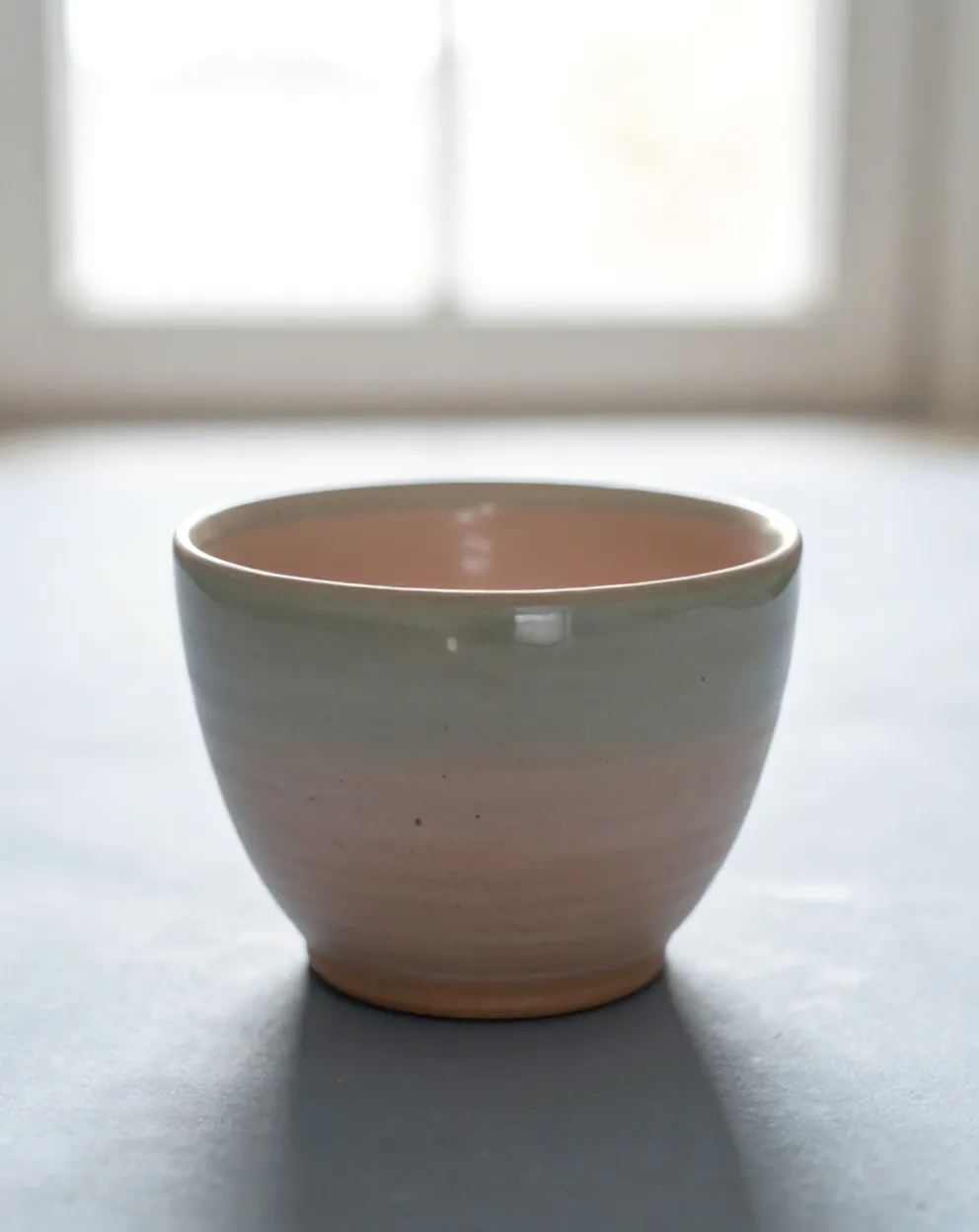 A blush stoneware cup with a thin pale rim, speckle and small drips