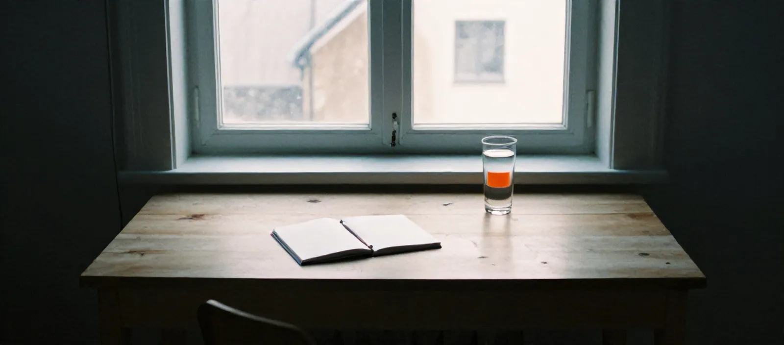 Pale birch desk by a tall window with a closed notebook and pencil in low winter sun