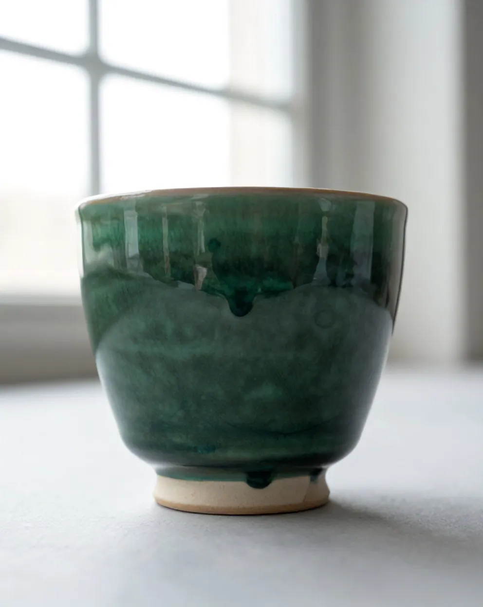 Close-up of green glaze pooling dark and glassy at the foot of a cup, above the raw clay ring