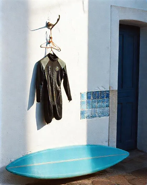 A wetsuit and surfboard by a whitewashed wall