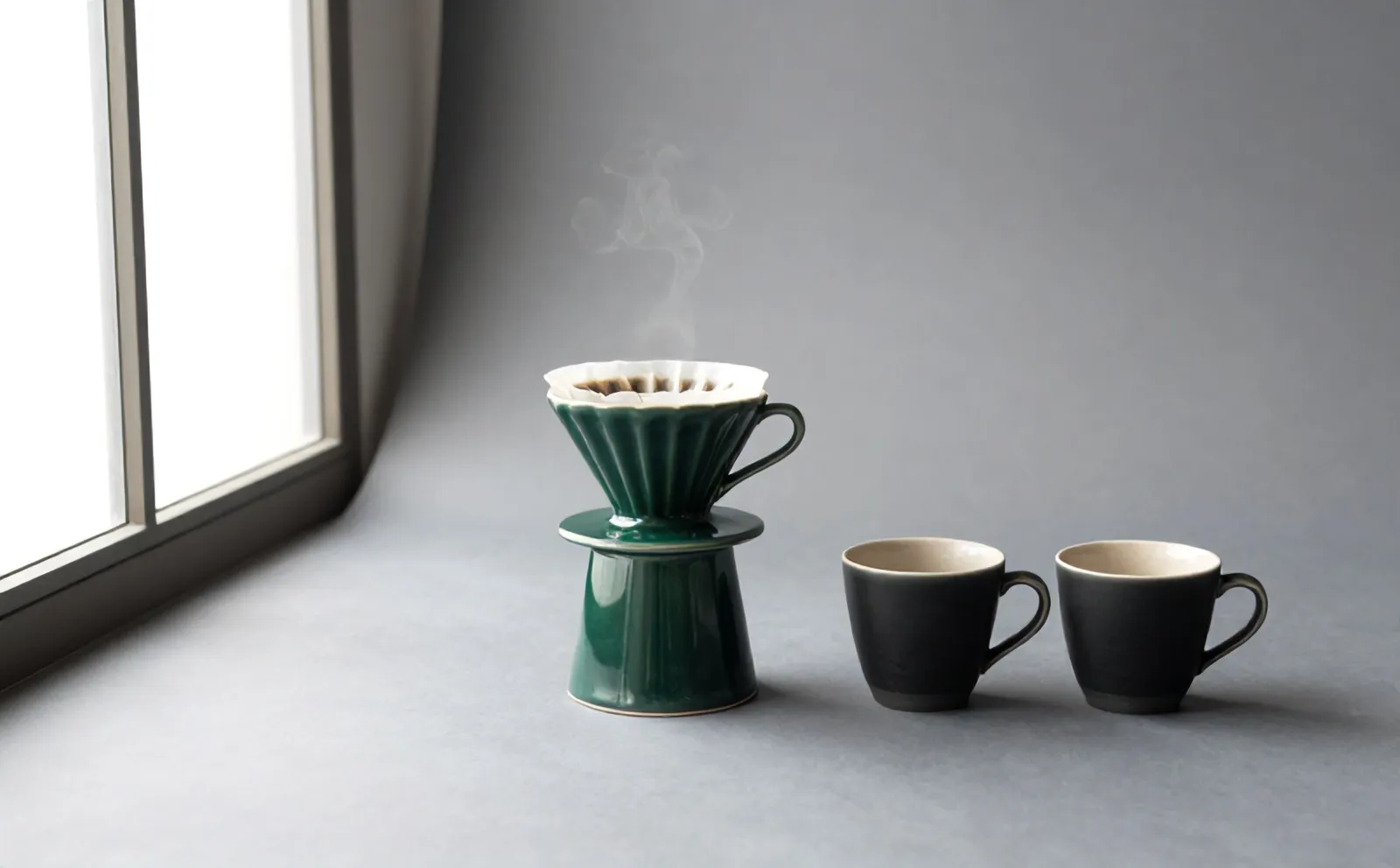 Coffee blooming in the green dripper above the carafe, two cups waiting in front